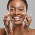 Portrait Of Happy Black Woman Applying Moisturizing Cream on Face